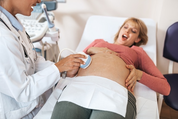 Mujer embarazada hermosa y feliz en el examen ginecológico con equipo médico de ultrasonido.