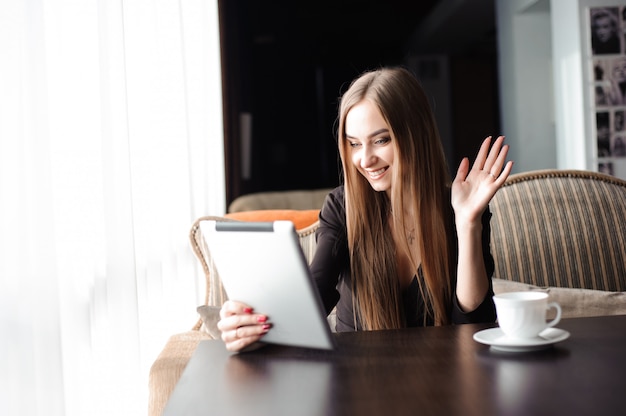 Mujer embarazada hermosa que usa la tableta digital en la tabla en café.