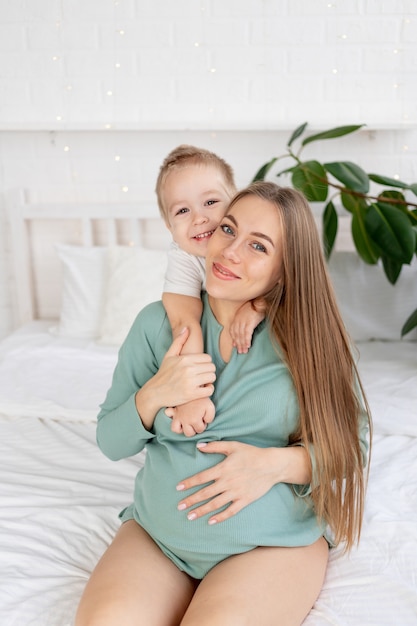 La mujer embarazada y el hijo toca una gran barriga en casa en la cama, el concepto de embarazo y la espera del nacimiento de un bebé y un segundo hijo en la familia.