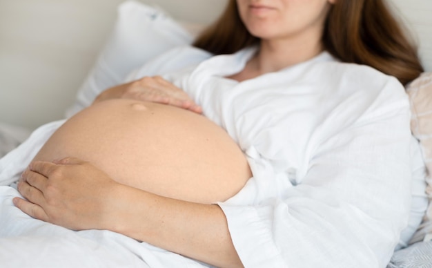 Mujer embarazada irreconocible acostada en la cama en casa acariciando acariciando la barriga del bebé Primer plano recortadoFeliz hermoso embarazoAmor por el futuro concepto de niño