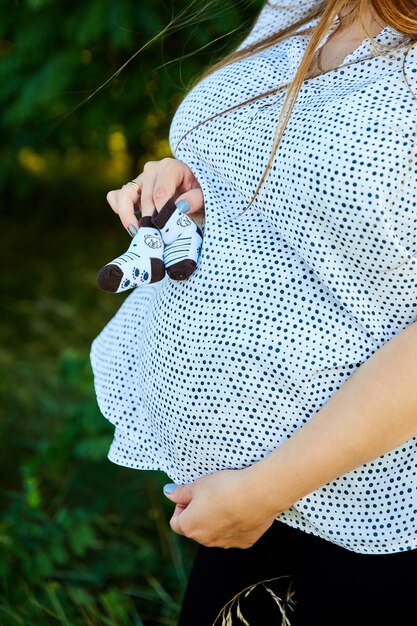 Mujer embarazada irreconocible tocando el vientre y sosteniendo zapatos de bebé