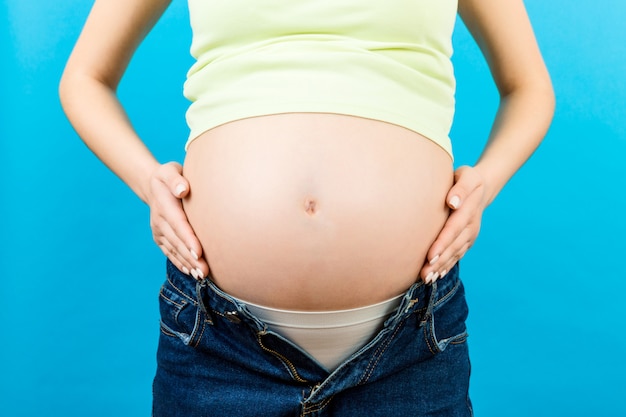 mujer embarazada en jeans abiertos acariciando su panza