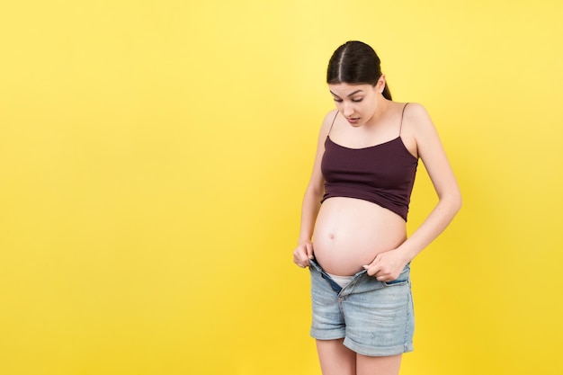 Mujer embarazada en jeans sin cremallera que muestra su vientre desnudo en un fondo colorido con espacio de copia Concepto de espera de bebé