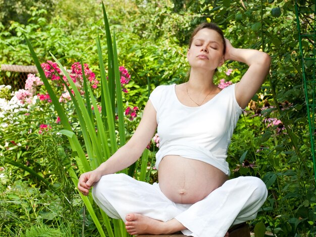Mujer embarazada joven que se relaja en un jardín de verano
