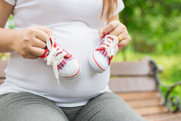 Mujer embarazada joven que sostiene los zapatos de bebé a su vientre