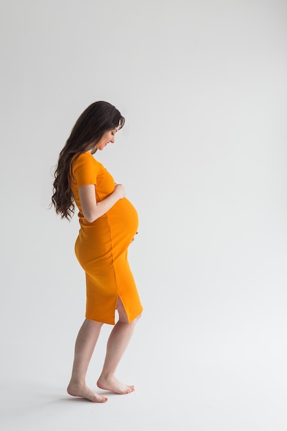 Mujer embarazada joven en vestido amarillo sobre fondo blanco.