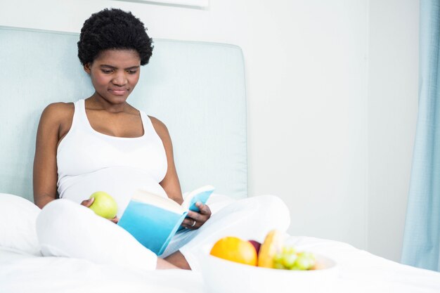 Mujer embarazada leyendo un libro acostado en su cama