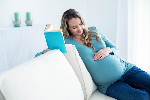 Mujer embarazada leyendo un libro en el sofá