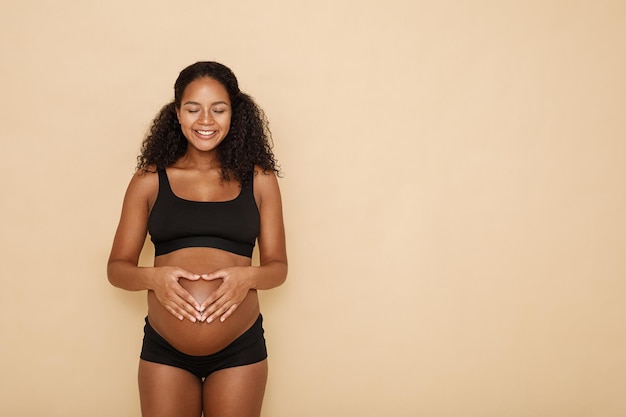Mujer embarazada con las manos en el vientre haciendo un símbolo de corazón