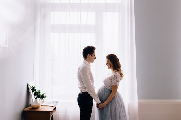 Mujer embarazada, con, marido, delante de la ventana