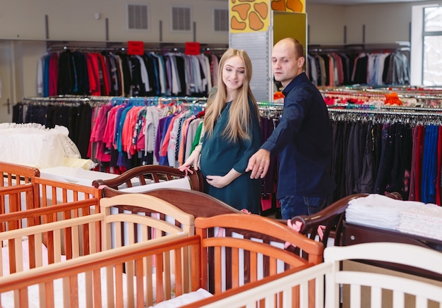 La mujer embarazada con el marido elige una cuna en la tienda.