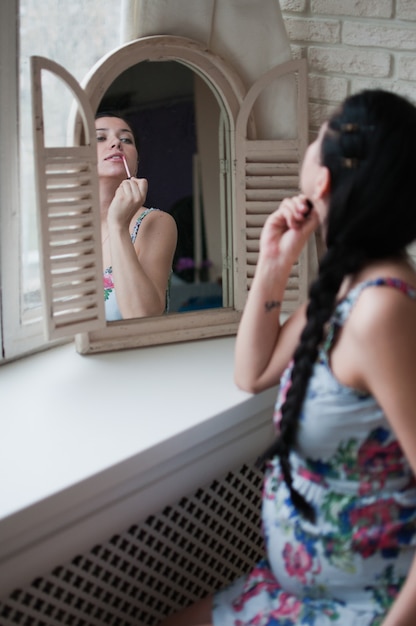 Mujer embarazada mira el espejo poniéndose maquillaje