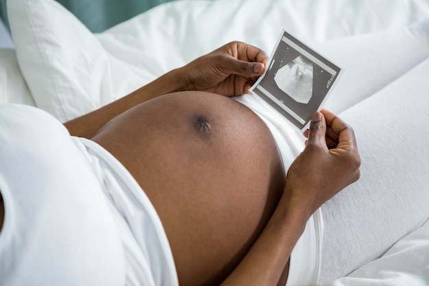 Mujer embarazada mirando imágenes de ultrasonido acostada en su cama