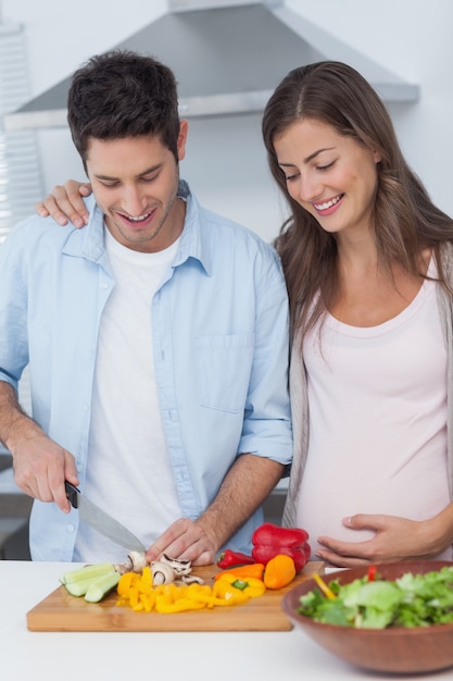 Mujer embarazada mirando marido cortar verduras