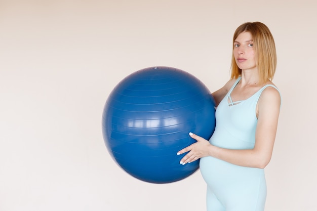 Mujer embarazada en mono azul con pelota de fitness en entrenamiento