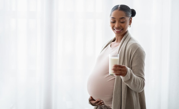 Mujer embarazada negra ofreciendo vaso con leche fresca ante la cámara