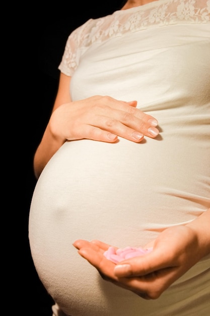 Una mujer embarazada con pastillas en la mano sobre un fondo negro