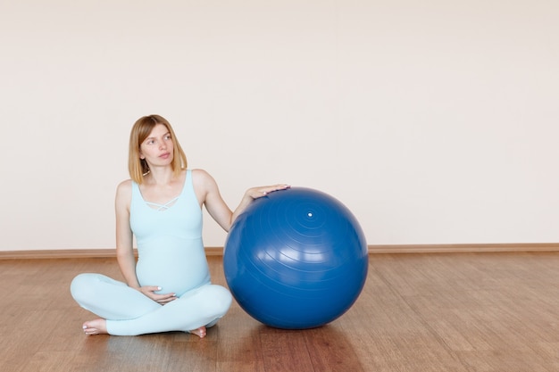 Una mujer embarazada con una pelota de fitness en el estudio. maternidad