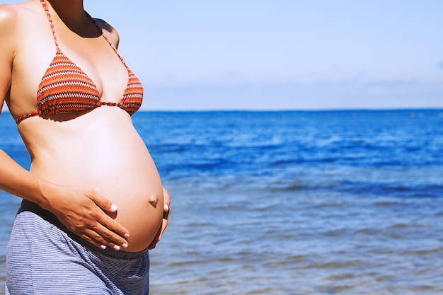 Mujer embarazada en la playa del mar en verano Primer plano de un hermoso vientre embarazado