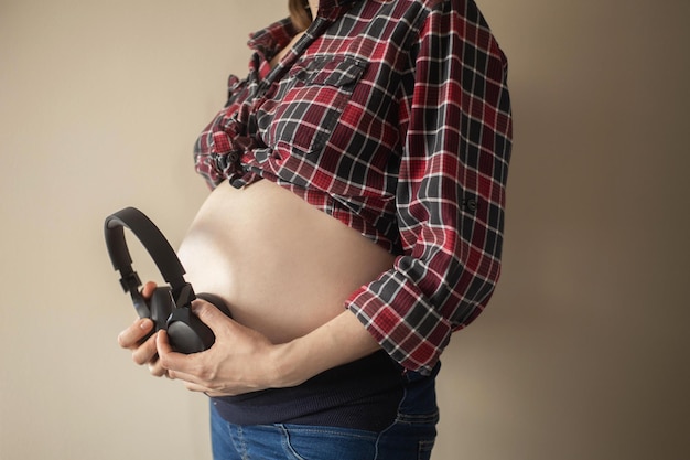 Una mujer embarazada se pone de perfil y se pone los auriculares en el estómago.