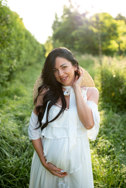 Mujer embarazada posando en un vestido blanco sobre un fondo de naturaleza