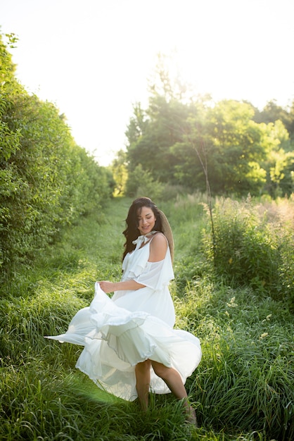 Mujer embarazada posando con un vestido blanco sobre un fondo de naturaleza.