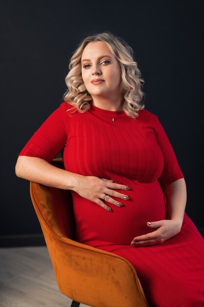 Mujer embarazada, posar, en, un, elegante, vestido rojo, interior, estudio, negro, pared, fondo, rubio, caucásico, mediana edad, hembra, seis meses, embarazo