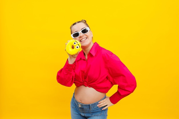 Mujer embarazada positiva comiendo donuts con camisa rosa aislada sobre fondo amarillo Felicidad del embarazo mientras espera un hijo Foto de alta calidad Alimentos nocivos durante el embarazo