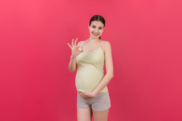 mujer embarazada positiva mostrando bien gesto contra su vientre en fondo de color embarazo fácil y feliz copiar espacio