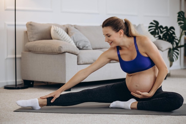 Mujer embarazada practicando yoga en casa en estera