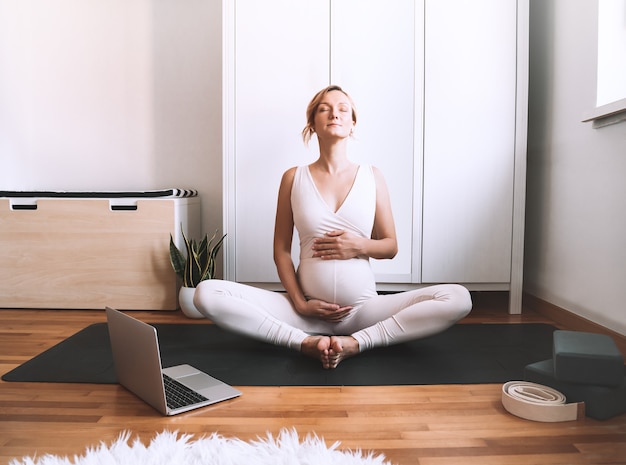 Mujer embarazada practicando yoga en casa con portátil Ejercicio femenino meditar durante el embarazo