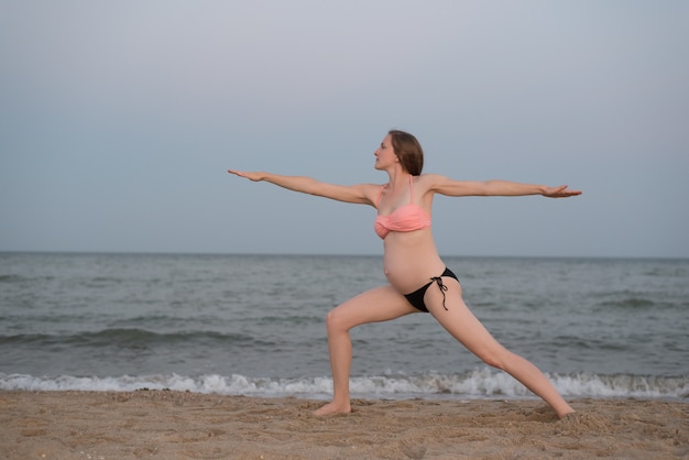 Mujer embarazada practicando yoga en la playa. Luz suave de la tarde