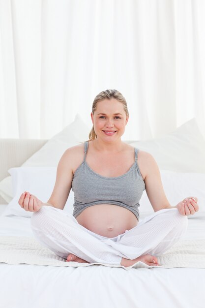 Mujer embarazada practicando yoga en su cama