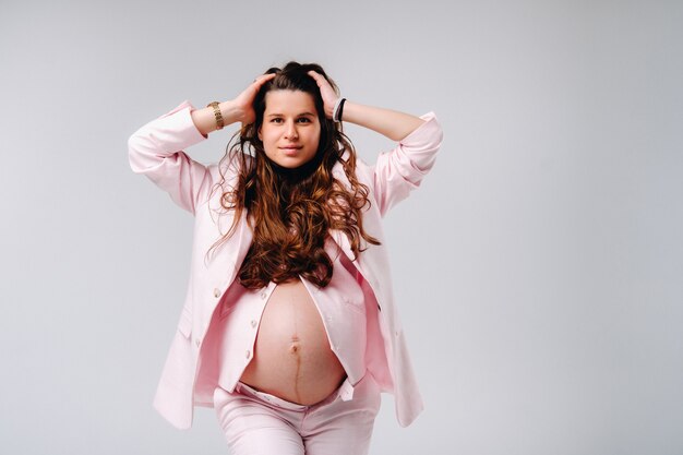 Mujer embarazada en primer plano de traje rosa sobre fondo gris.
