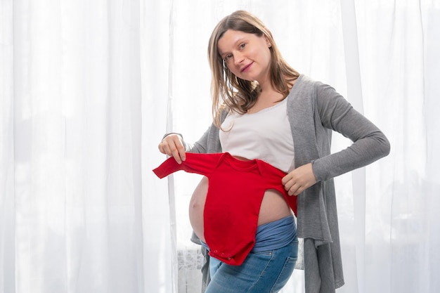 Una mujer embarazada probando monos rojos en su vientre presente para un bebé en unboxing de baby shower