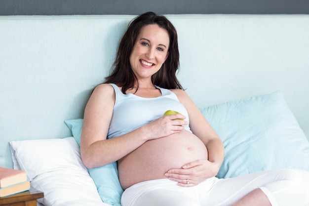 Mujer embarazada que sostiene una manzana en su vientre en casa