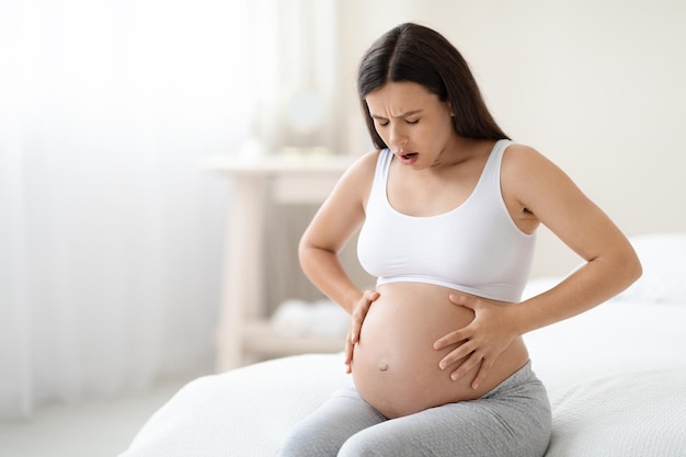Mujer embarazada que sufre de dolor abdominal en el espacio de copia en casa
