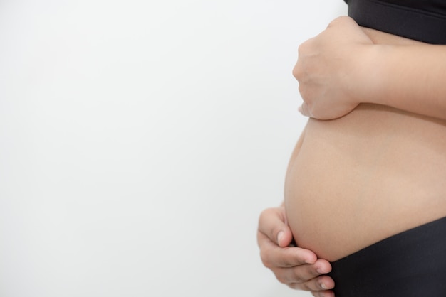 Mujer embarazada que toca su panza con cuidado en el fondo blanco.