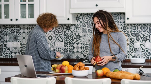 Mujer embarazada con rastas y su marido rizado en la cocina moderna detrás de la cocina fresca y