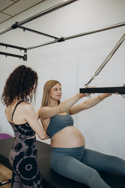 Mujer embarazada reformador de pilates ejercicio de cadillac con entrenador personal