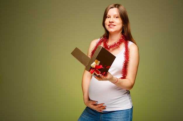 Mujer embarazada con un regalo expresión de la cara sorprendida que se presenta en la víspera de Navidad