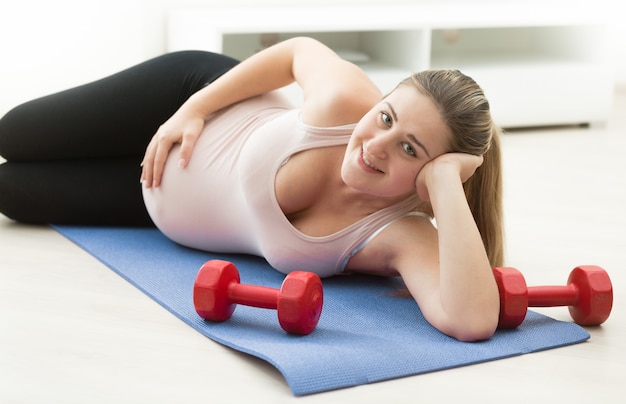 Mujer embarazada relajándose en la colchoneta de fitness después de hacer ejercicio