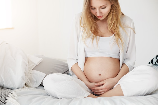 Foto mujer embarazada relajándose en su dormitorio disfrutando de la maternidad sosteniendo su vientre pateando.