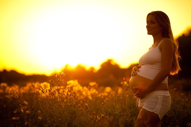 Mujer embarazada en ropa blanca, en el campo durante la puesta de sol