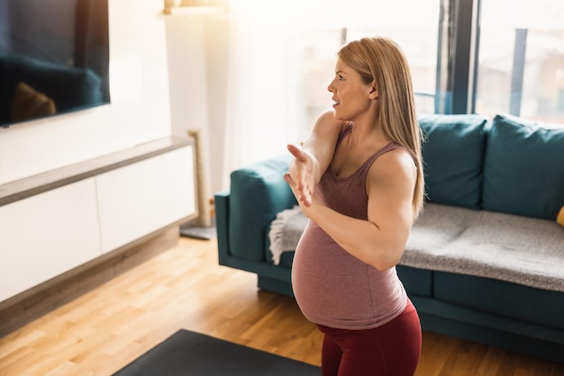 Una mujer embarazada con ropa deportiva se estira y hace ejercicio para promover el bienestar en su sala de estar.