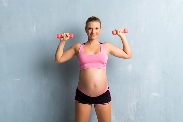 Mujer embarazada rubia haciendo deporte haciendo levantamiento de pesas