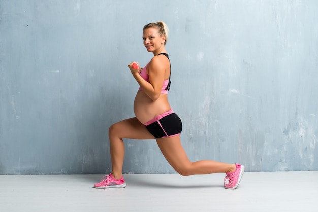 Mujer embarazada rubia haciendo deporte haciendo levantamiento de pesas