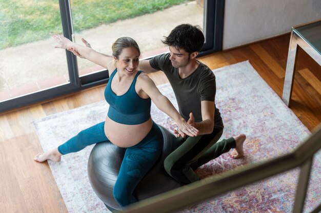 Mujer embarazada rubia practicando yoga con su pareja en la sala de estar en casa