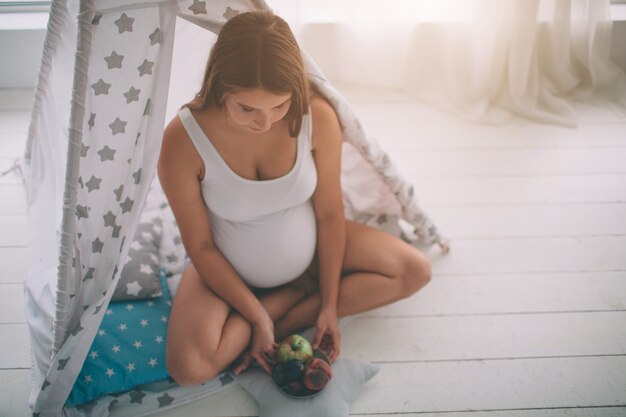 Mujer embarazada saludable comiendo fruta en la habitación de los niños en la habitación de los niños.