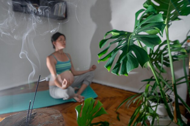 Mujer embarazada sentada en una colchoneta de yoga en una pose de meditación Mujer embarazada haciendo ejercicios de yoga en casa Sala de incienso para relajarse durante el yoga Yoga durante el embarazo